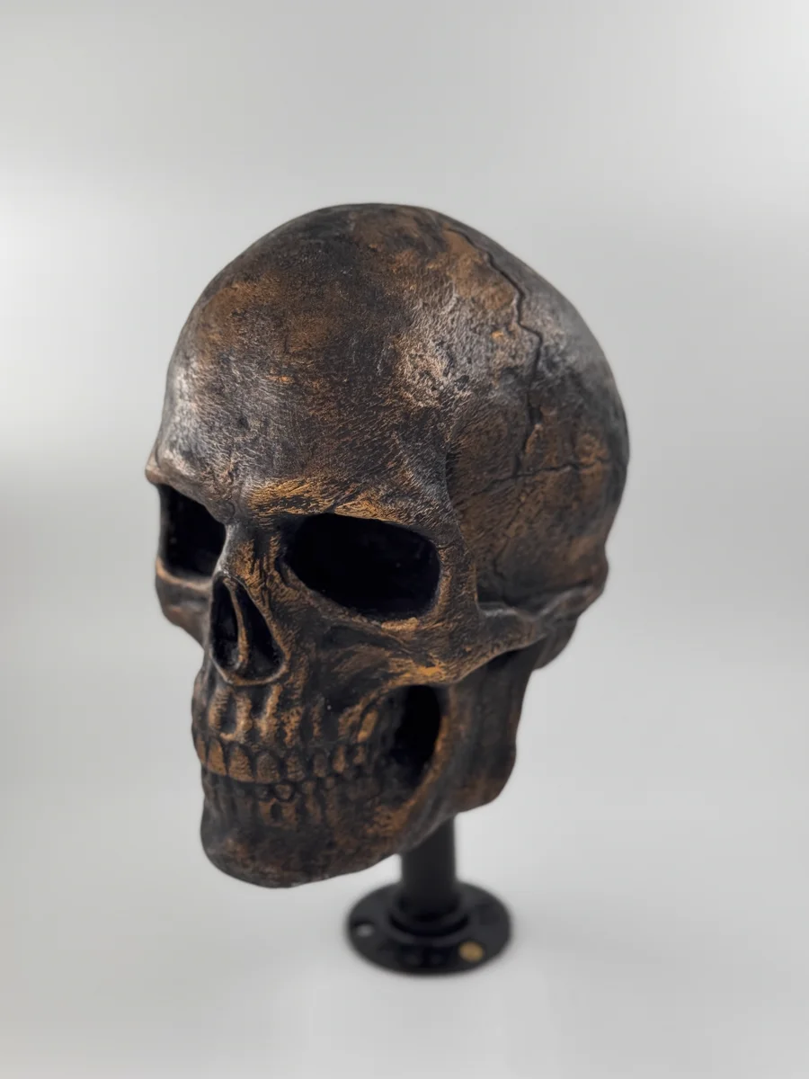 Un crâne décoratif imprimé en 3D, finition bronze vieilli, posé sur un petit socle noir