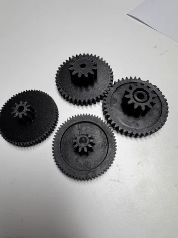 Quatre engrenages noirs imprimés en 3D, posés sur une table claire