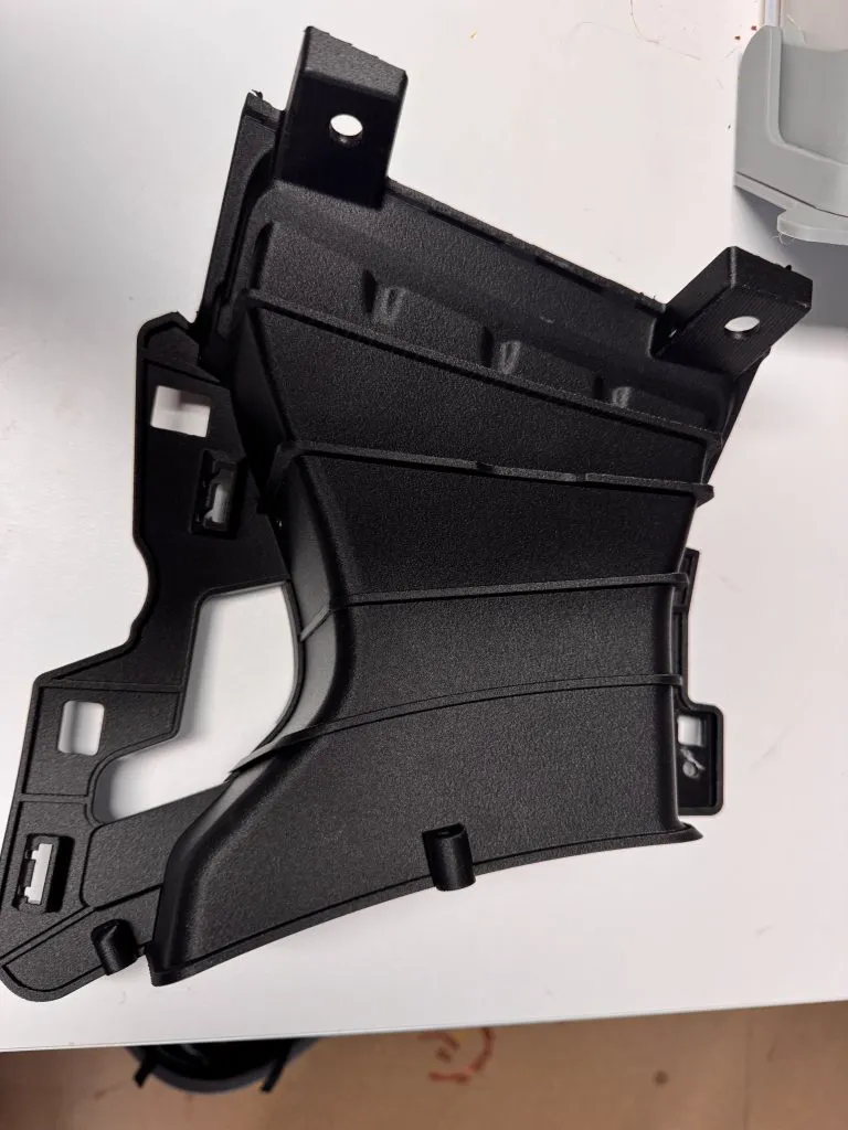 Une pièce noire de carrosserie automobile imprimée en 3D, de forme nervurée, avec ses découpes et ses pattes