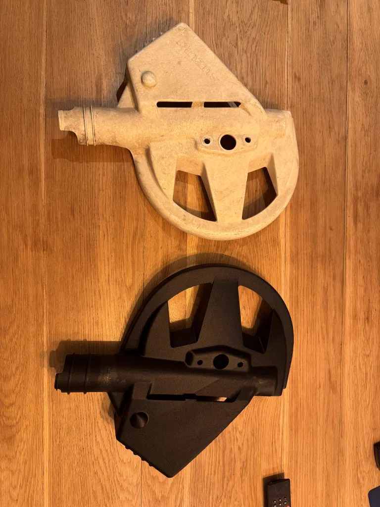 Une pièce d’origine claire et cassée, posée sur du bois à côté de sa copie noire imprimée en 3D