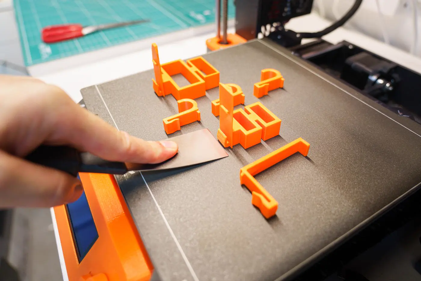 Une main décolle à la spatule des pièces orange imprimées en 3D, posées sur un plateau gris