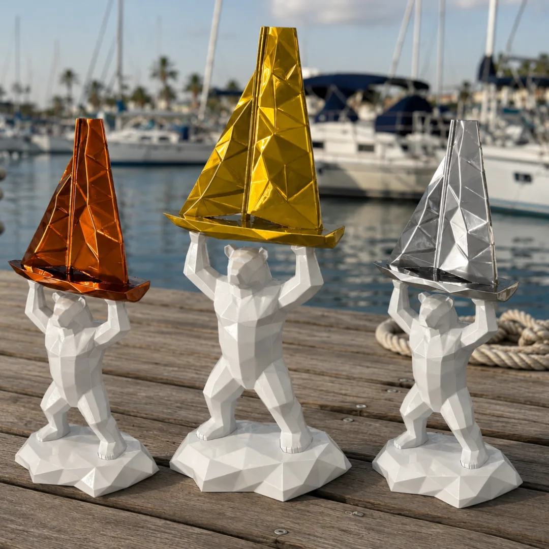 Trois trophées imprimés en 3D : un ours blanc à facettes qui soulève un voilier bronze, or ou argent